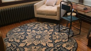 A corner room with a beige armchair, a glass table with a notebook, and a patterned rug on a wooden floor. - Cozy Seward Home - Close To Everything (Minneapolis)