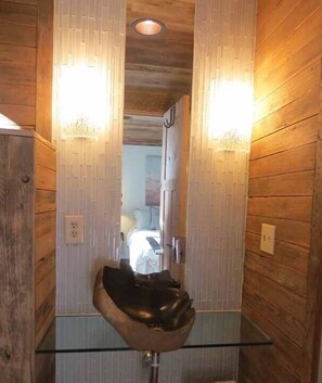 Un baño con paredes de madera, un lavabo de cristal y dos luces fijadas a la pared.