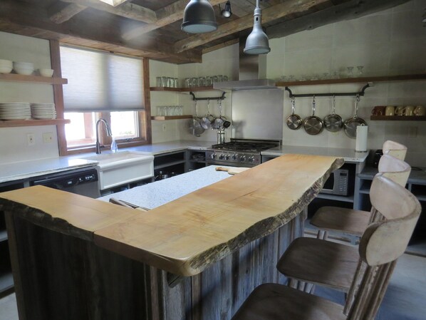 Una cocina rústica con una isla de madera, taburetes de bar, una estufa y ollas colgantes.