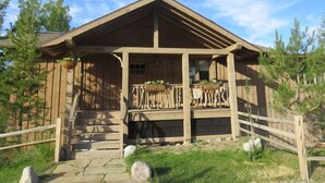 Een houten chalet met een veranda, het cijfer '1005' op de deur, en een stenen trap die erheen leidt.