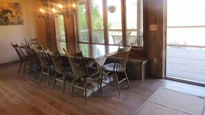 Een eetruimte met houten tafels en stoelen, grote ramen en uitzicht op het omliggende landschap.