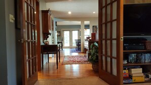 A spacious living area with a wooden floor, a dining table, chairs, a bookshelf, and a television. - Charming Home quiet neighborhood lovely back yard 5 min from Garden of Gods (Colorado Springs)