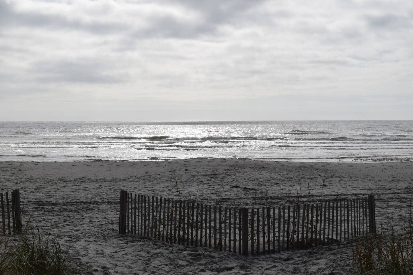 Een strand met een houten omheining op de voorgrond en de oceaan op de achtergrond.