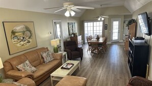 A spacious living room with a brown leather sofa, a coffee table, and a dining area with wooden chairs and a table. - Clean Beach House on 2nd row easy access to beach! (Cherry Grove)