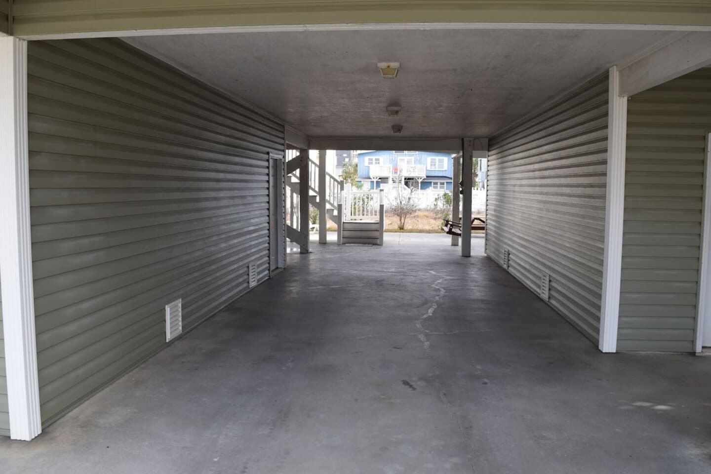 A covered outdoor area with closed metal shutters on both sides, a concrete floor, and a view of buildings in the background.