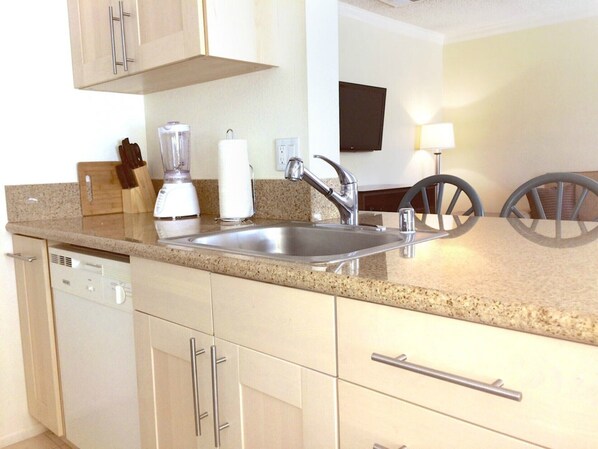 A kitchen with a granite countertop, stainless steel sink, and white cabinets.