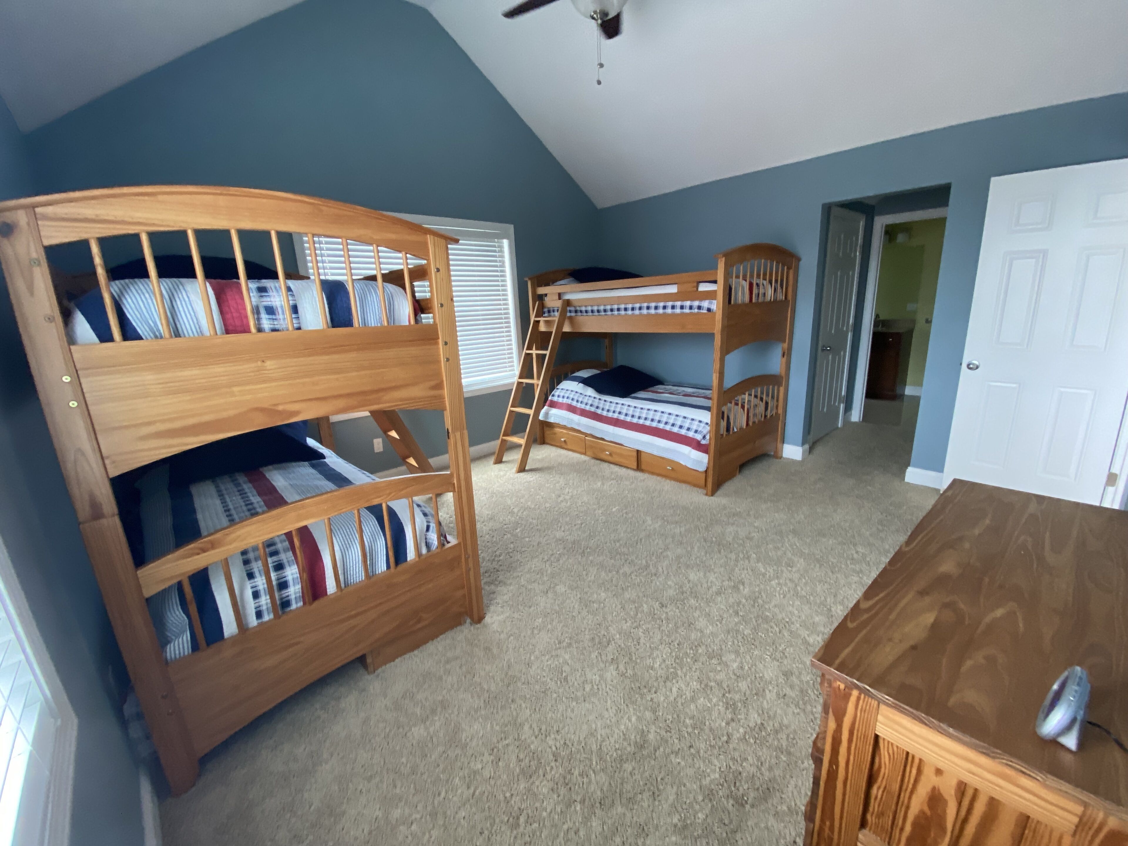 Une chambre avec des lits superposés, une commode en bois et un ventilateur de plafond.