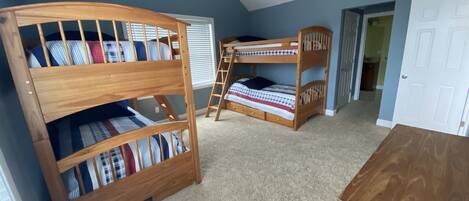 Une chambre avec des lits superposés, une commode en bois et un ventilateur de plafond.