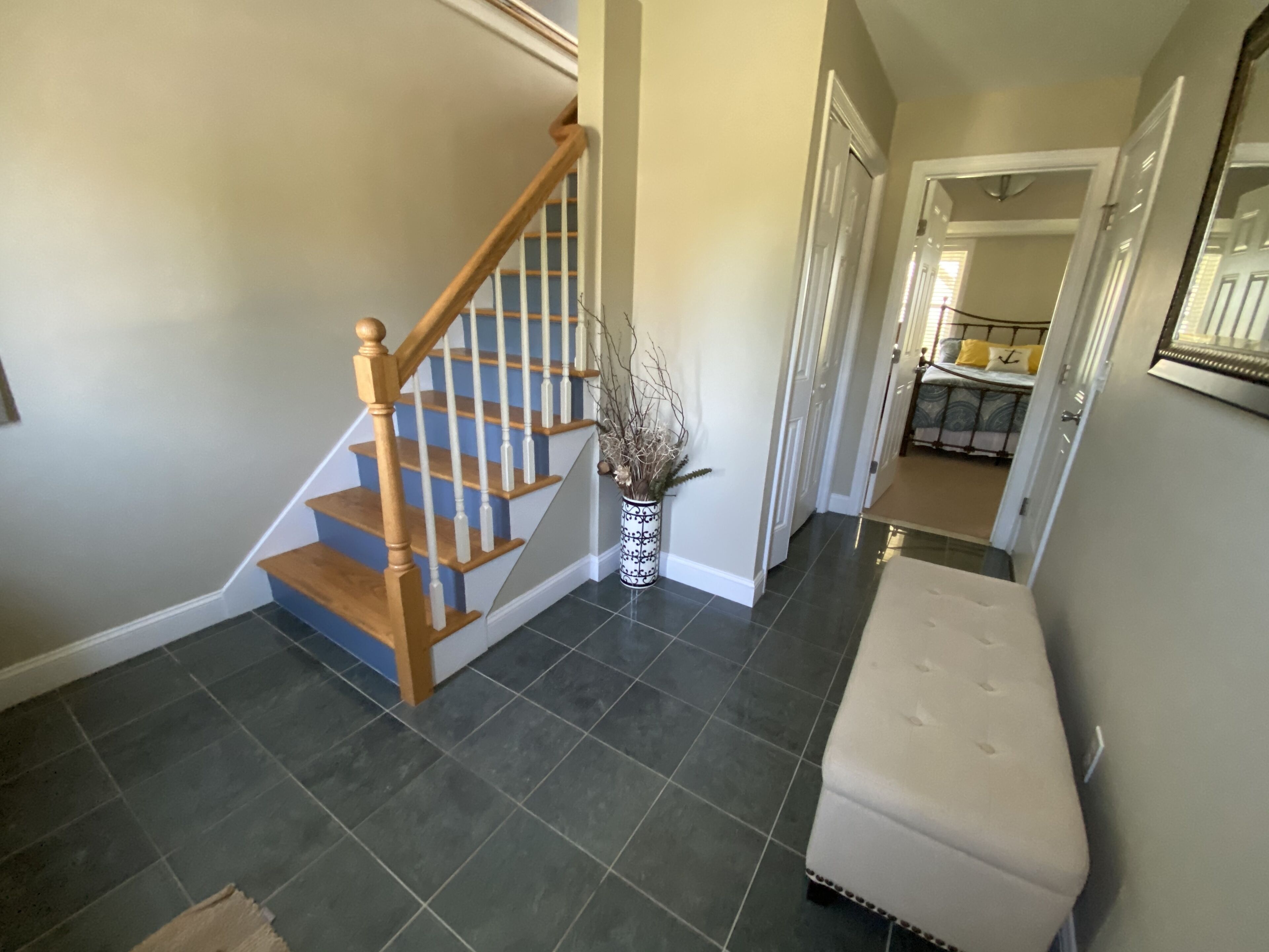 A staircase with wooden steps and white balusters, a white bench, and a vase with dried plants.