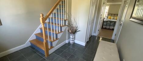 A staircase with wooden steps and white balusters, a white bench, and a vase with dried plants.