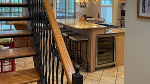 Una cocina moderna con una isla central, una escalera de madera y ventanas amplias.