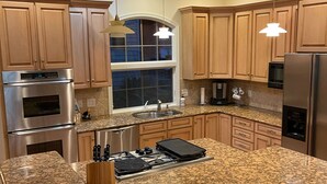 Una cocina moderna con encimeras de granito, electrodomésticos de acero inoxidable, armarios de madera e iluminación colgante.