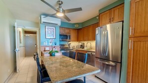 A kitchen with a granite countertop, stainless steel appliances, wooden cabinets, and a ceiling fan. - Beachfront Mana Kai Maui Unit #502 (Kihei)