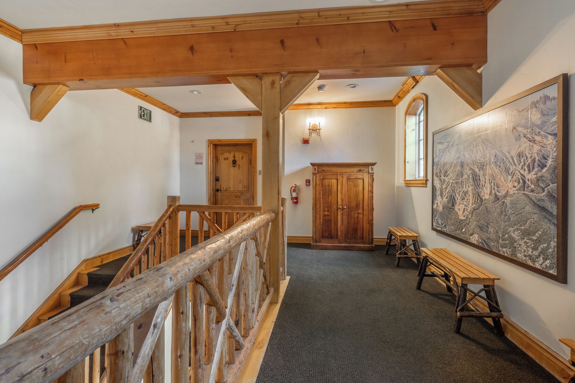 A wooden staircase with a railing, a wooden door, a fire extinguisher, and a large framed map on the wall.