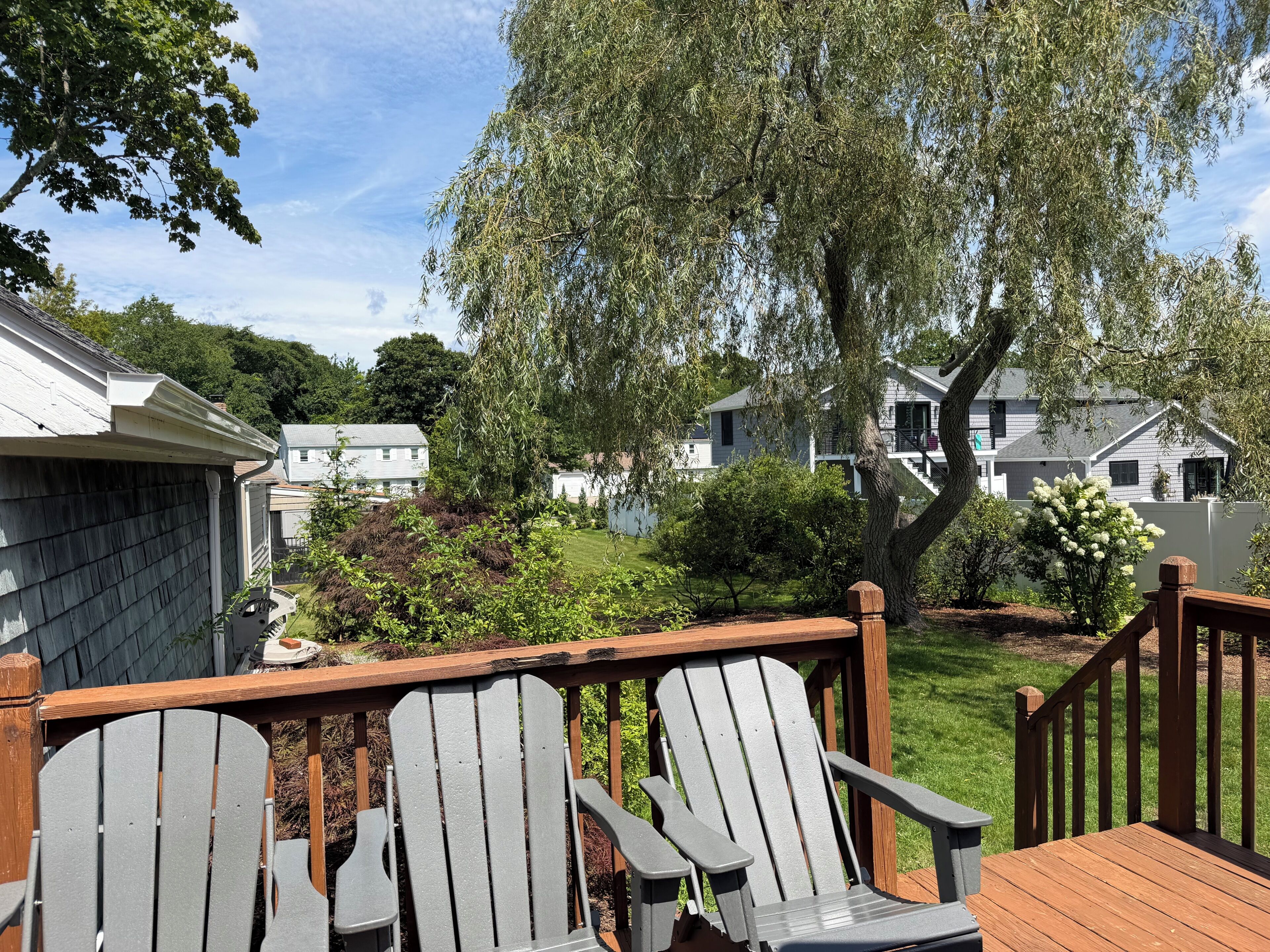 Eine Terrasse mit Adirondack-Stühlen, einem Holgitter und Blick auf eine Wohngegend mit Häusern und Bäumen.