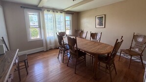 Comedor con mesa y sillas de madera, ventanas amplias con cortinas y una lámpara en el techo.