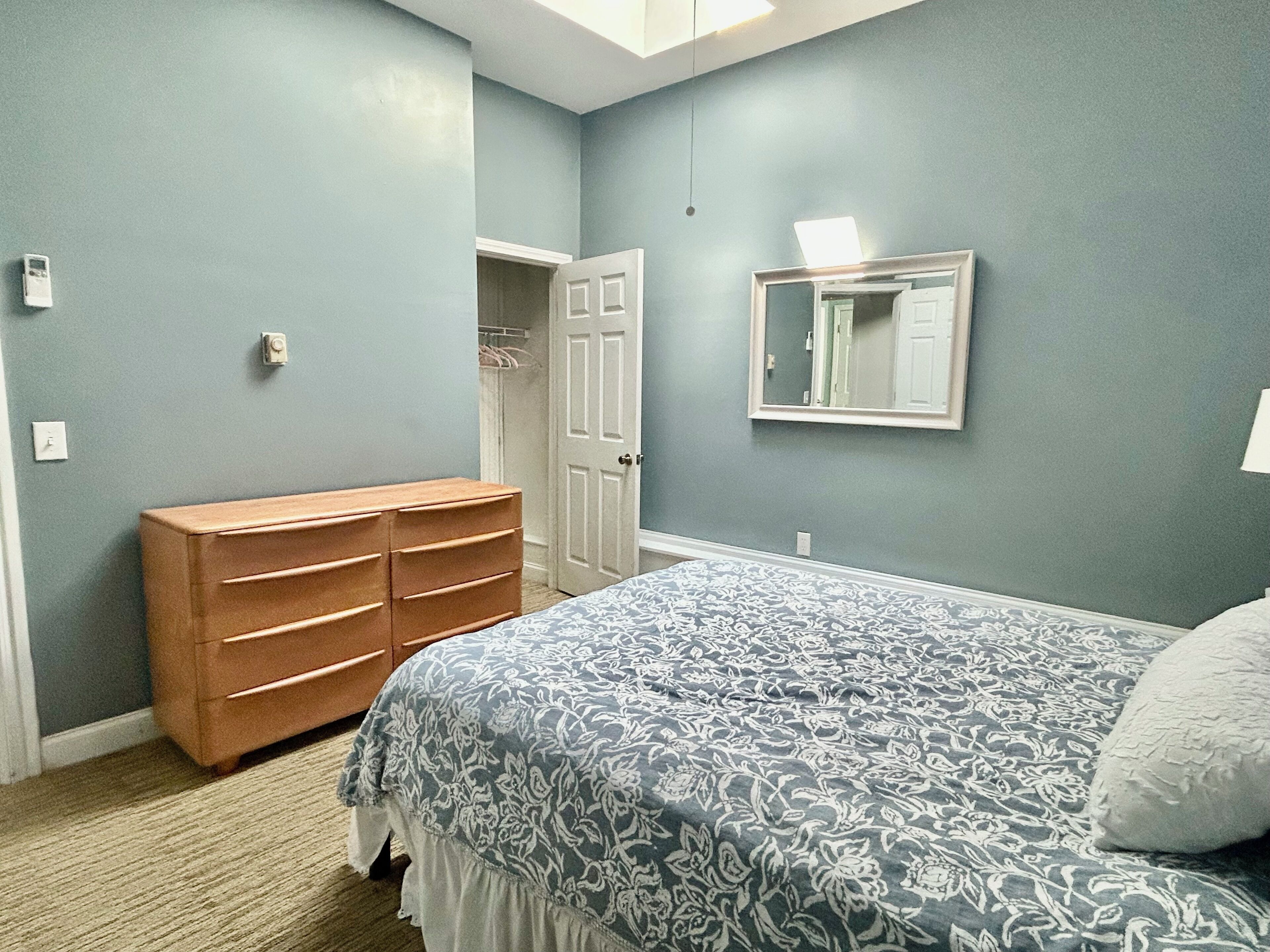 Un dormitorio con cama, cómoda, armario y espejo en la pared.