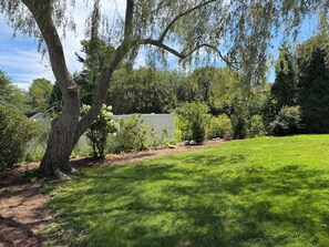 A residential property with a well-maintained lawn, mature trees, and a white building.