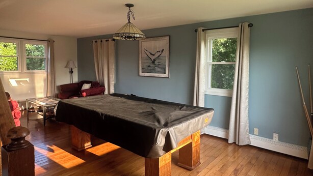 Una habitación con mesa de billar, un sillón rojo, una lámpara y un cuadro en la pared.