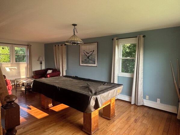 A room with a pool table, a red armchair, a lamp, and a painting on the wall.