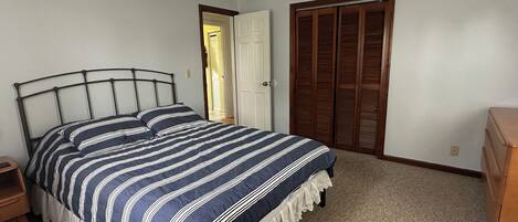 Een slaapkamer met een bed, nachtkastje, dressoir, plafondventilator en een deur naar een andere kamer.