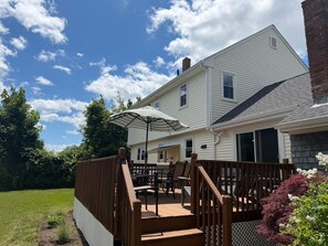 Uma casa de dois andares com varanda, móveis de exterior e um guarda-sol grande.