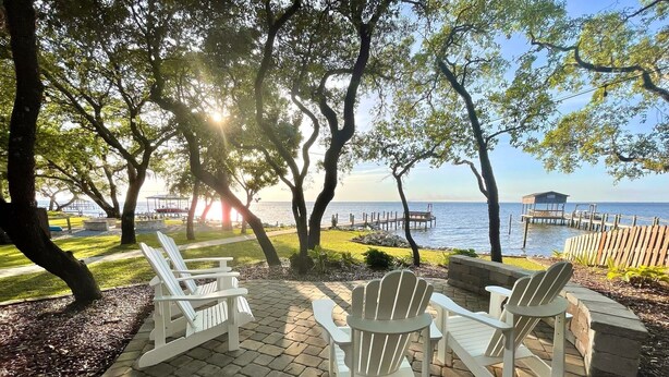 Un patio con sillas Adirondack que da a un cuerpo de agua y un muelle.
