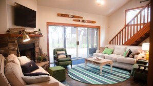 Una sala de estar con chimenea, televisor, escalera y puerta corrediza de vidrio que da a un patio trasero.