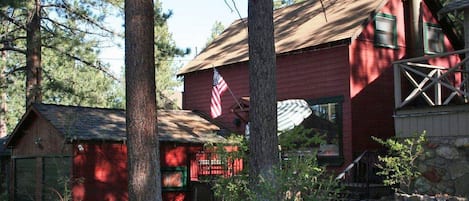 A red wooden cabin with a thatched roof, surrounded by trees and a stone wall.