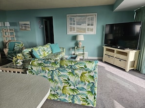 Uma sala de estar com sofá, televisão e uma pequena mesa com abajur.