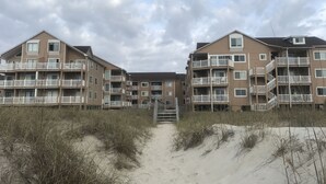 Ein Apartmentkomplex direkt am Strand, mit mehreren Balkonen und einem Sandweg zum Eingang.