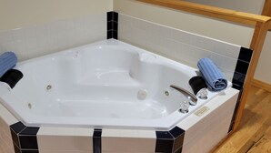 Eine große, weiße, freistehende Badewanne mit schwarz-weißen Fliesen darumherum.