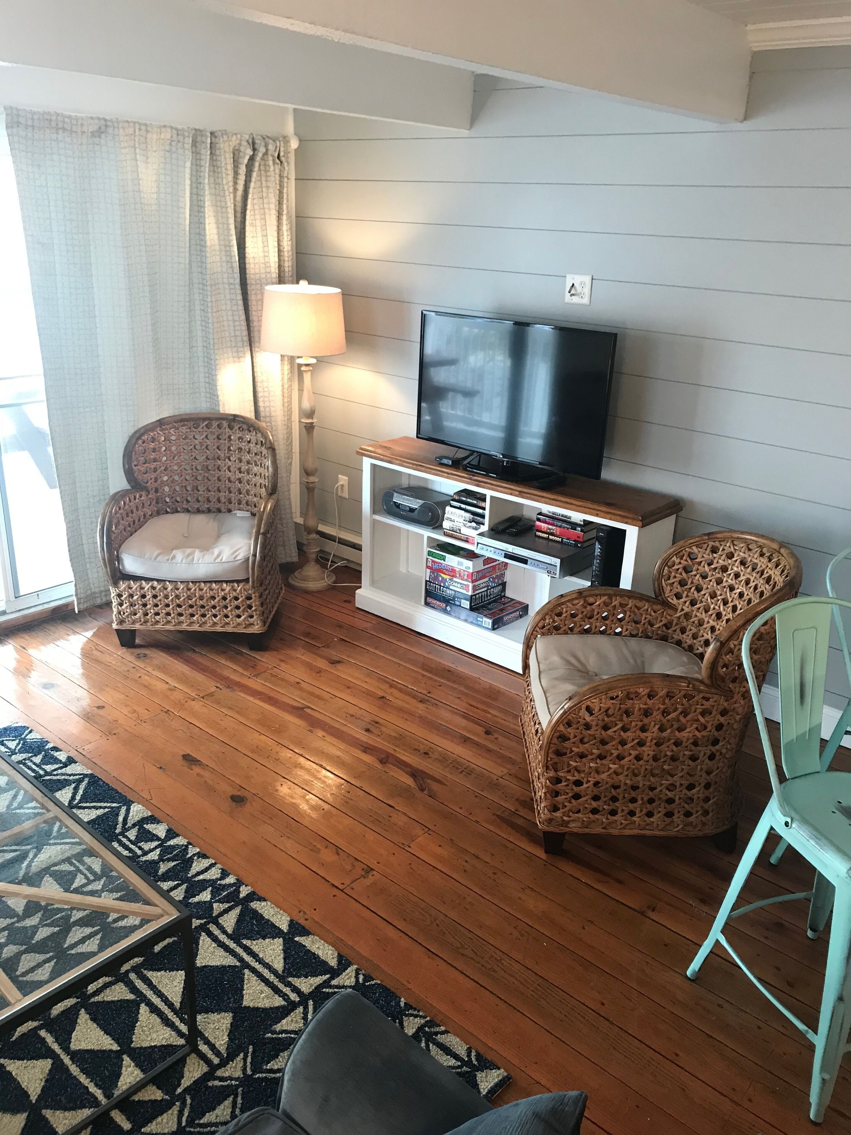 A living room with a television, wicker chairs, a bookshelf, and a patterned rug.