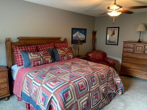 Un dormitorio con una cama de madera, una silla roja, un aparador de madera y un ventilador de techo.