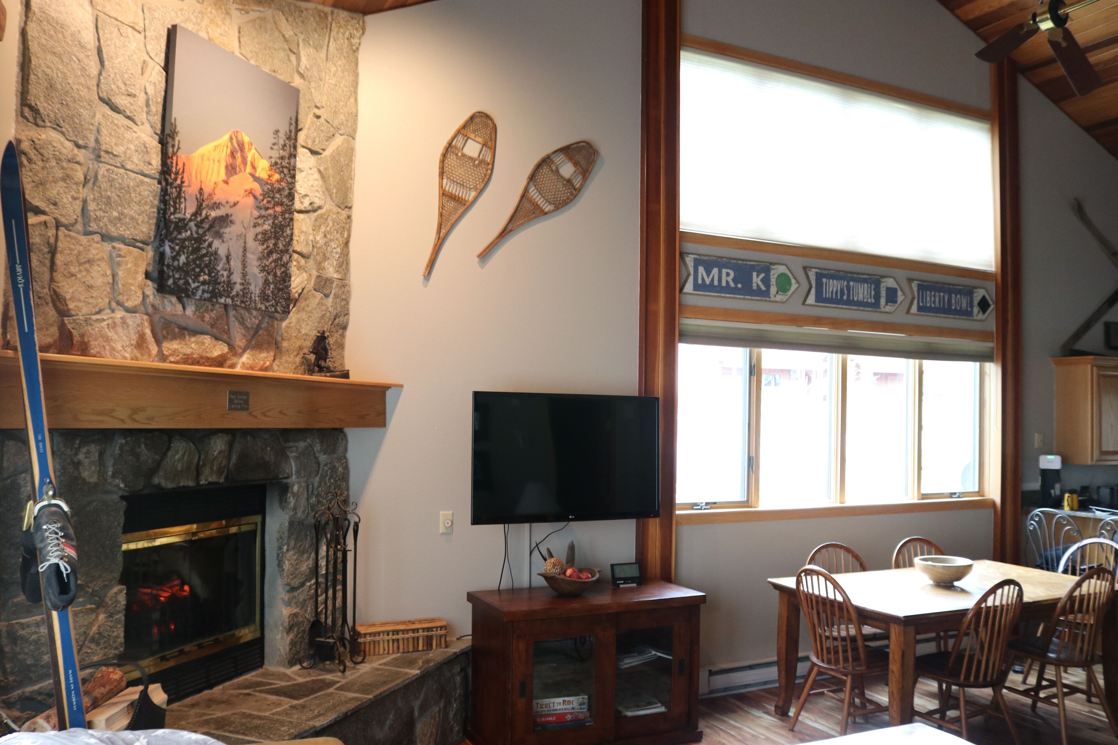 Una habitación acogedora con chimenea de piedra, televisor y comedor con sillas de madera.