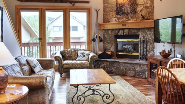 A cozy living room with a stone fireplace, leather sofa, wooden coffee table, and a television. - Ski In/Ski out - Great Location in Big Sky Mountain Village (Big Sky)