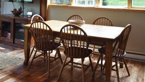 A dining area with a wooden table and chairs, a television, and a window with a view of a house and trees. - Ski In/Ski out - Great Location in Big Sky Mountain Village (Big Sky)
