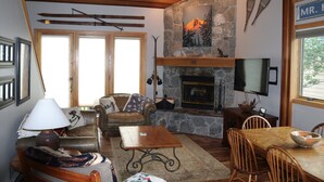 A cozy living room with a stone fireplace, wooden furniture, and a television mounted on the wall. - Ski In/Ski out - Great Location in Big Sky Mountain Village (Big Sky)
