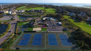 Vista aérea de una zona residencial con varias canchas de tenis, un campo de golf y una masa de agua al fondo.