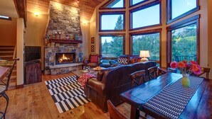 A cozy living room with a stone fireplace, leather sofa, and large windows offering a view of the forest. - Million Dollar Views on Lake Purgatory! Only 1 Mile to Ski Resort! (Durango)