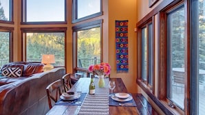 A dining area with a wooden table, benches, and a chandelier. Large windows provide views of the outdoors. - Million Dollar Views on Lake Purgatory! Only 1 Mile to Ski Resort! (Durango)