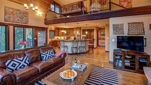 A spacious living area with a leather sofa, a dining table with oranges, a kitchen in the background, and a balcony with a railing. - Million Dollar Views on Lake Purgatory! Only 1 Mile to Ski Resort! (Durango)
