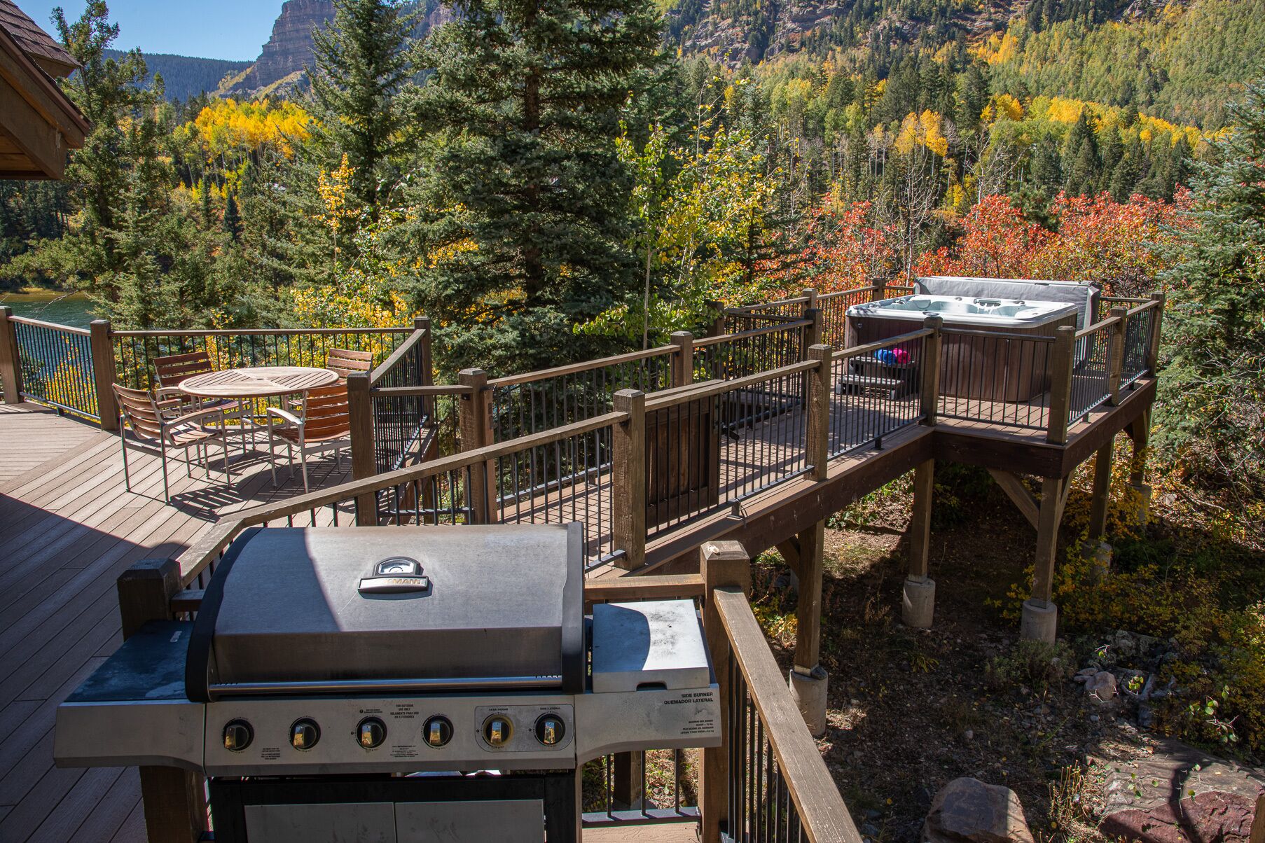 A deck with a grill, seating, and hot tubs overlooking a forested area.