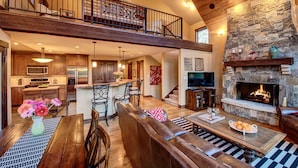 A spacious loft-style living area with a stone fireplace, a dining area with a wooden table and chairs, and a kitchen with modern appliances. - Million Dollar Views on Lake Purgatory! Only 1 Mile to Ski Resort! (Durango)