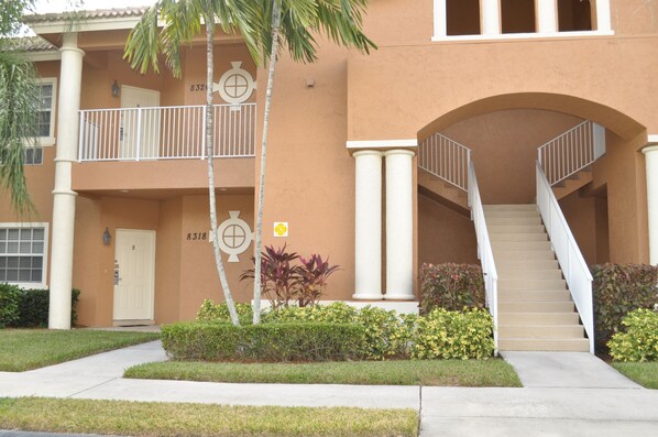 A two-story building with a beige facade, white columns, and a central staircase.