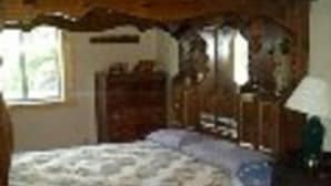 Een slaapkamer met een houten bed, een sprei en een dressoir.