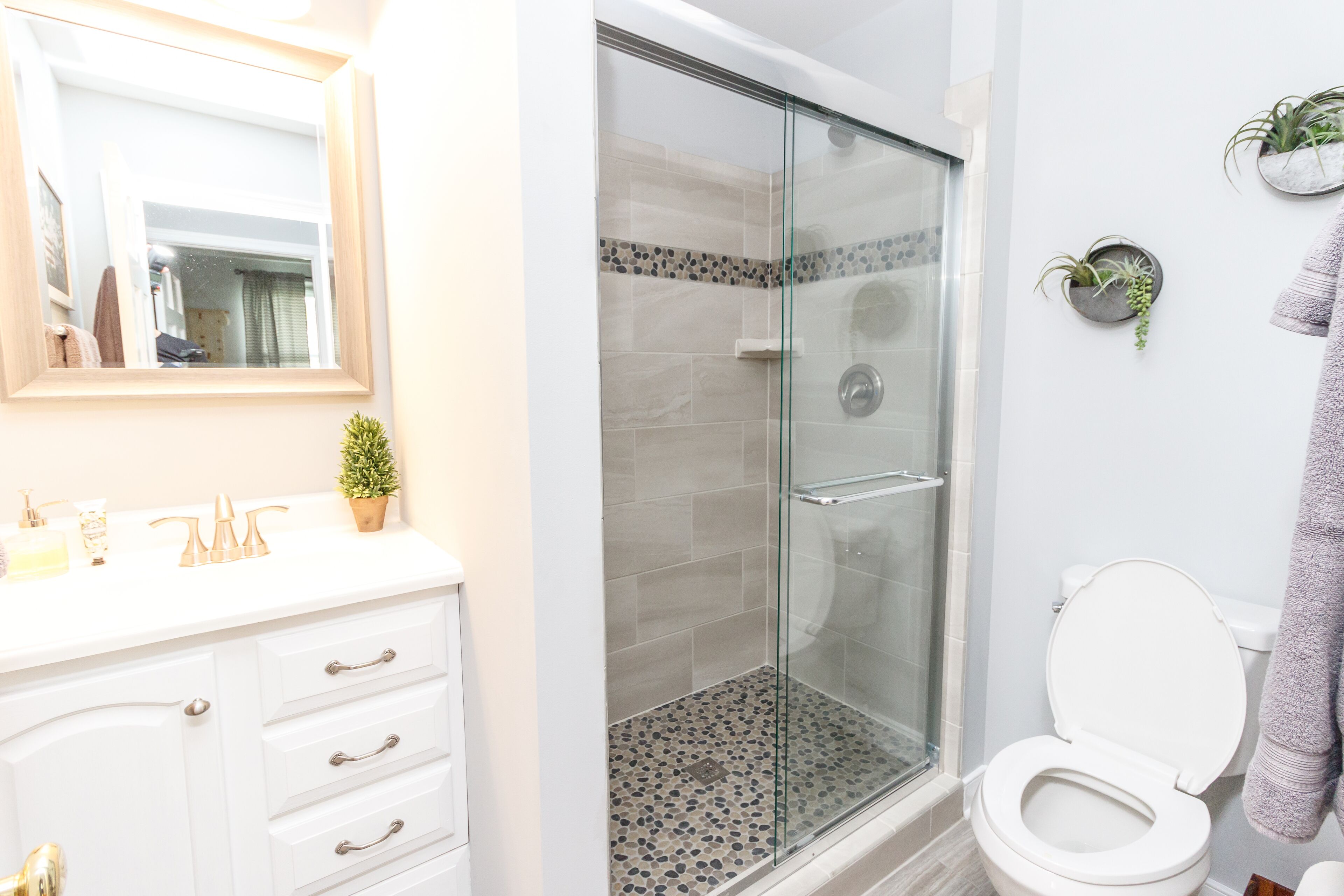A bathroom with a glass-enclosed shower, a white sink with gold fixtures, and a toilet.