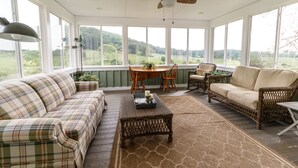 A sunroom with a large window, a ceiling fan, a sofa, a wicker chair, and a dining table. - Relax in the beautiful South River Valley just minutes from wineries,  (Stanardsville)