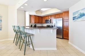 Una cocina con armarios de madera, una isla central con taburetes de bar, un refrigerador y un microondas.