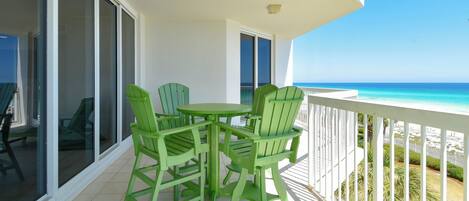 Een balkon met een tafel en stoelen, uitzicht op de oceaan en een witte reling.